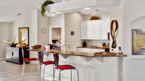 A modern kitchen with a central island, bar stools, and a dining area.