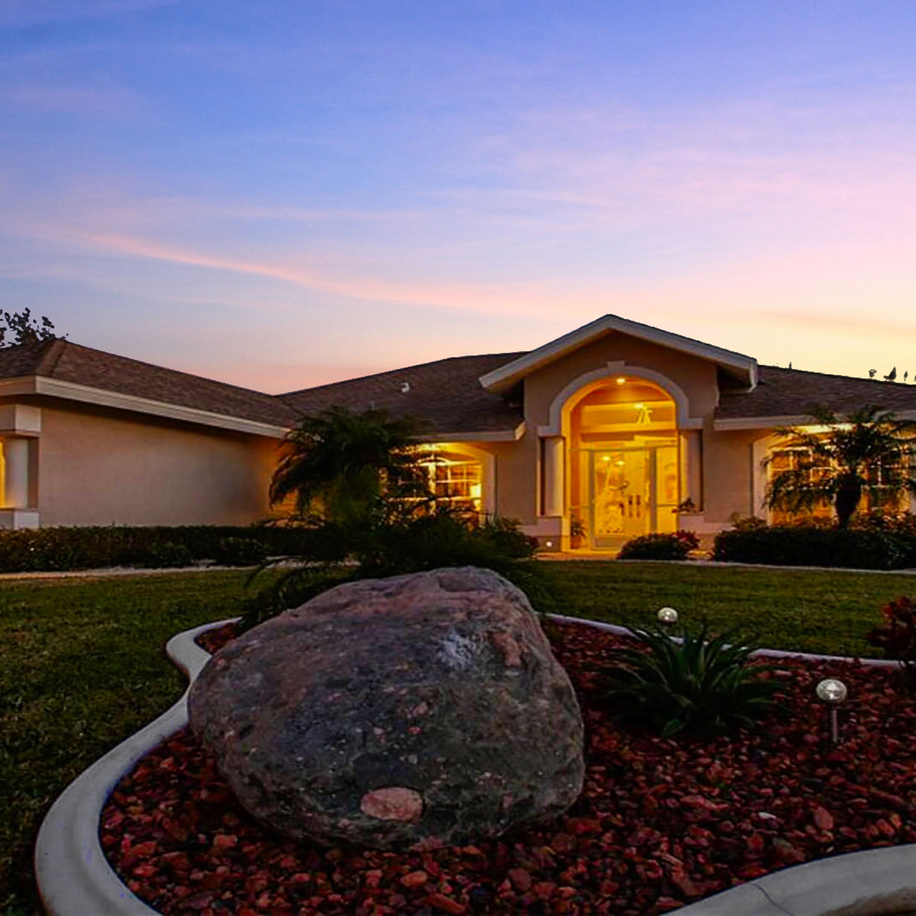 A house with a large rock in the front yard, a well-maintained lawn, and a clear sky.