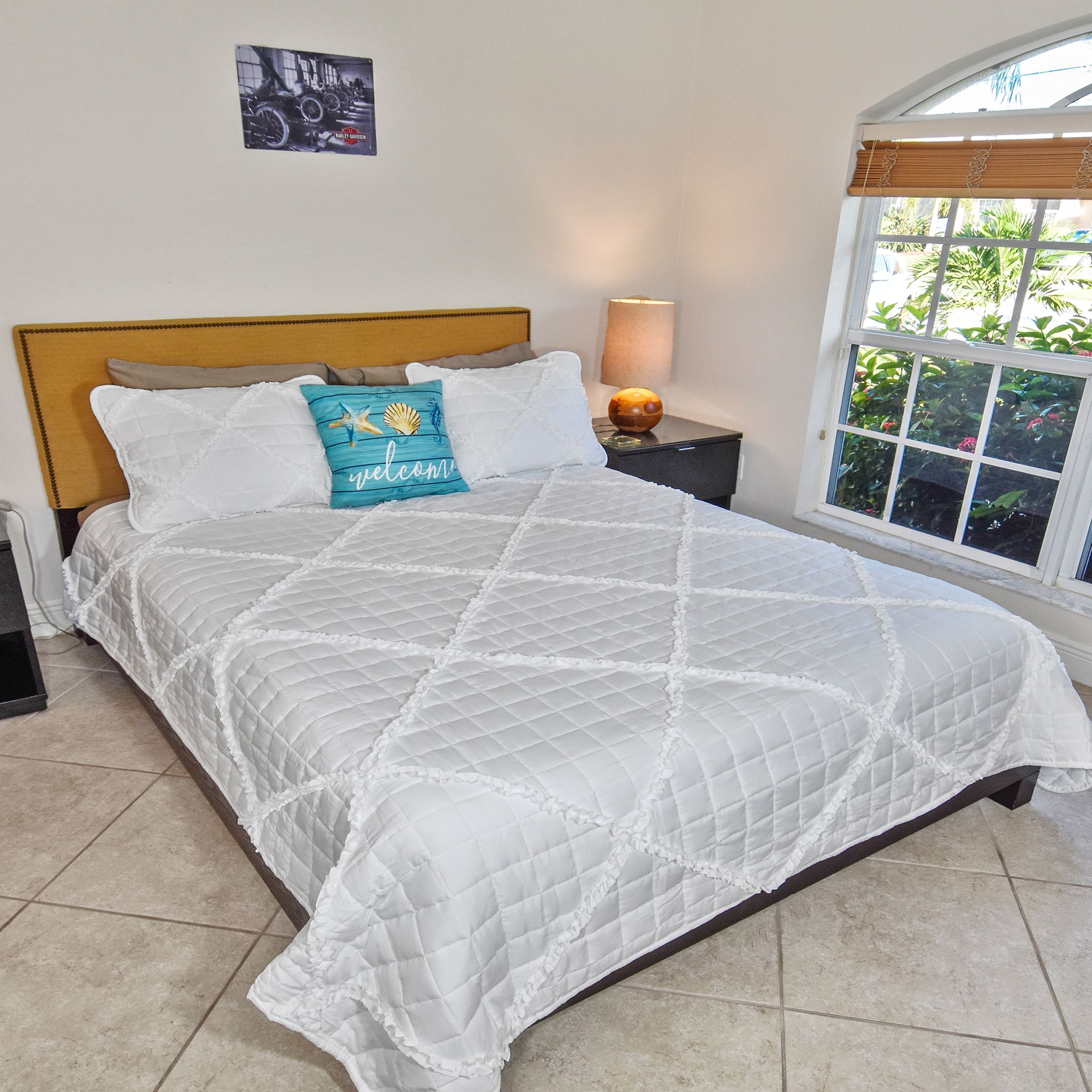 A bed with a white quilted bedspread, a wooden headboard, and a pillow with a seashell design.