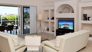 A spacious living room with a large TV, white sofas, a coffee table, and a ceiling fan.