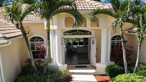 A building with a covered entrance, palm trees, and a paved pathway leading to the entrance.