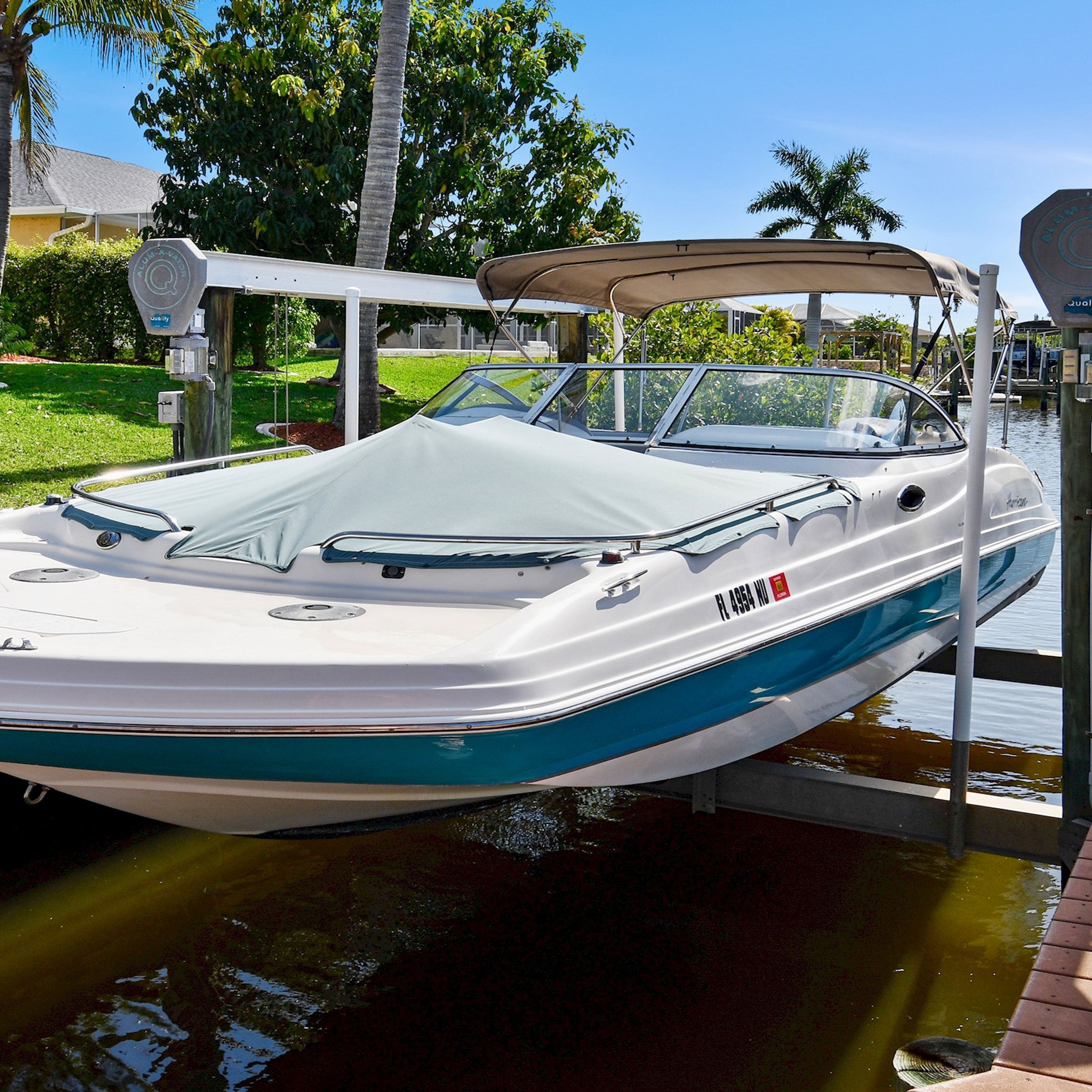A white and blue boat docked at a marina with a canopy, surrounded by greenery and a clear sky.