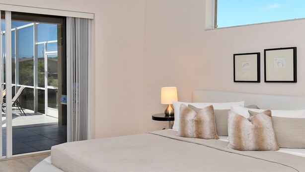 A modern bedroom with a curved white sofa bed, a bedside table with a lamp, and two framed pictures on the wall.