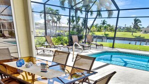 A glass-top table with chairs, a pool, and a view of palm trees and a grassy area. - Timeout -south Facing With Large Terrace and Pool (Cape Coral)