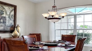 A dining room with a large table, chairs, a chandelier, and a window with a view of greenery. - Timeout -south Facing With Large Terrace and Pool (Cape Coral)