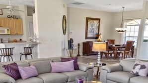 A living room with a grey sofa, a glass coffee table, and a patterned rug. There is a dining area with a wooden table and chairs in the background. - Timeout -south Facing With Large Terrace and Pool (Cape Coral)