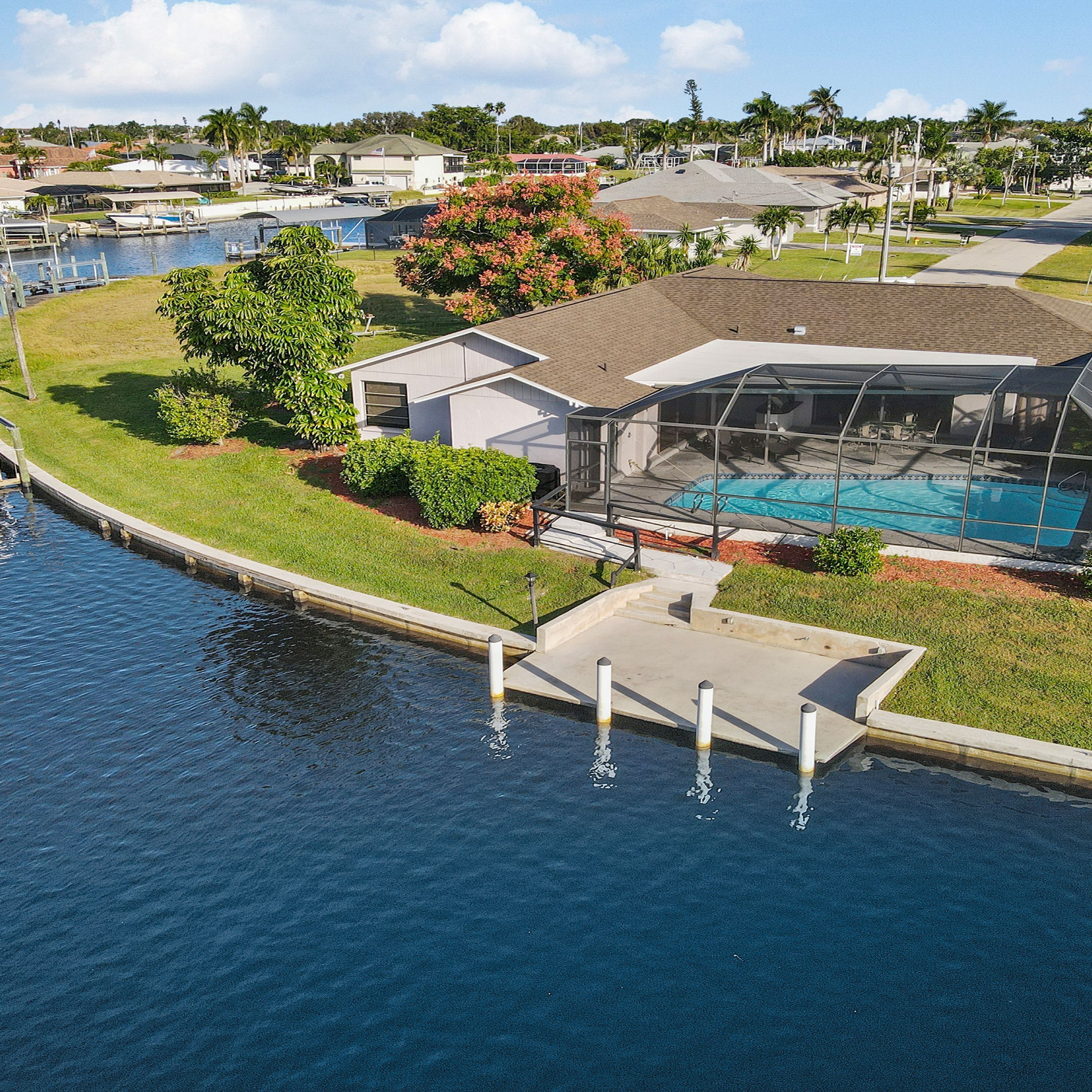 Ein Wohnhaus mit Swimmingpool, überdachter Terrasse und einer anlegbaren Mole, die ins Wasser ragt.