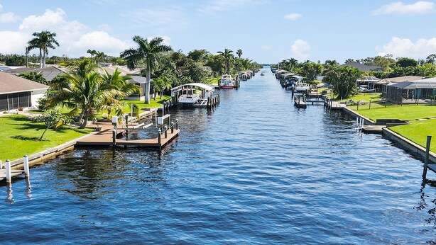 A canal with boats docked on both sides, surrounded by greenery and residential buildings. - Belle Paradise - 3 3 Pool Boating Oasis of Calm (Cape Coral)