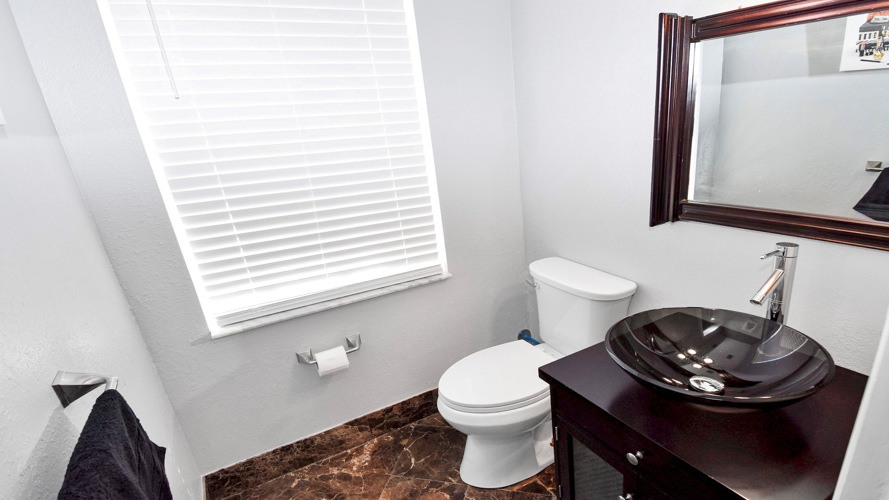 Ein Badezimmer mit Toilette, Waschbecken mit Spiegel und Fenster mit Jalousien.