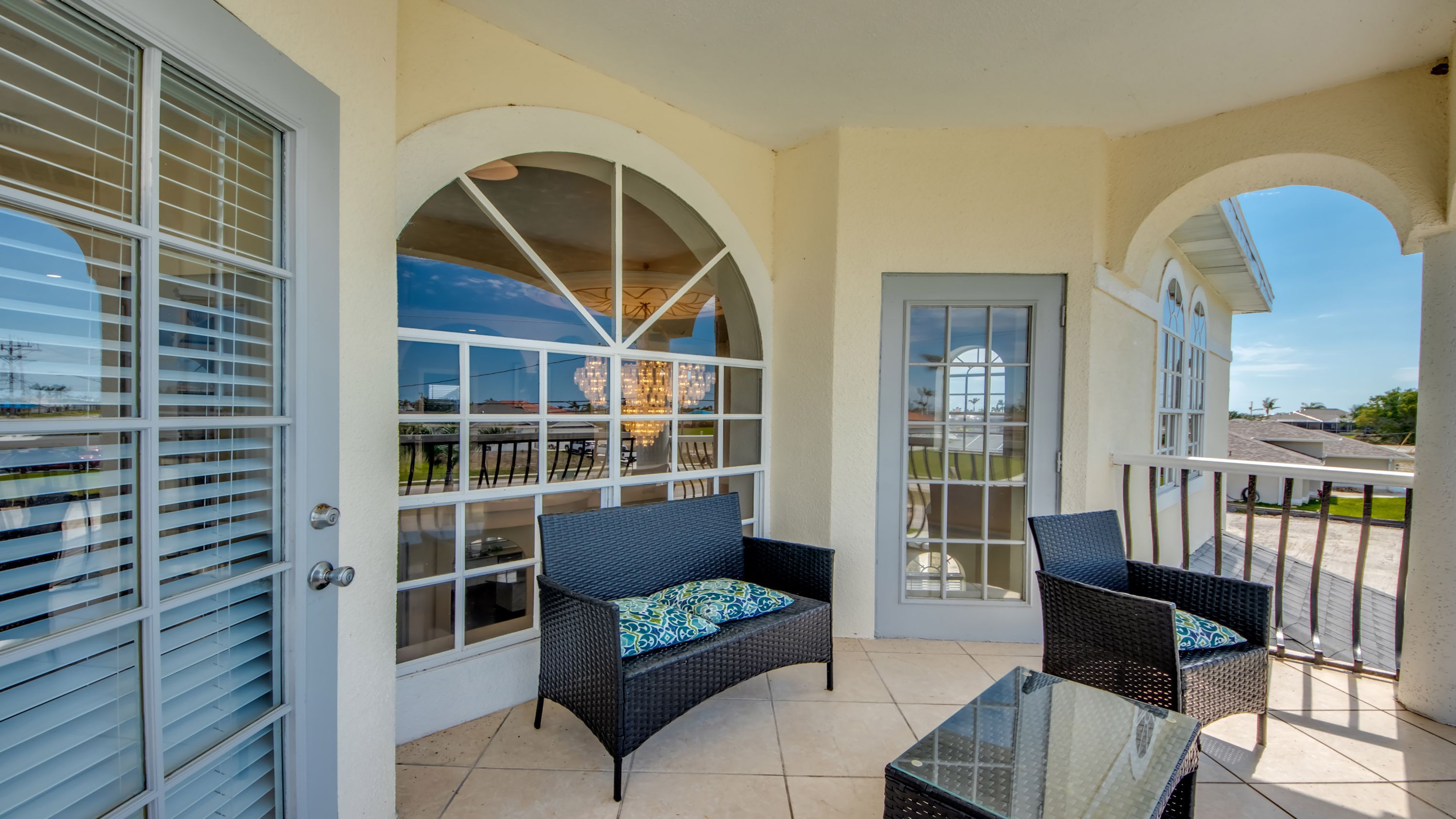 Un patio techado con mobiliario de mimbre, una mesa de vidrio y vistas a un área de comedor con iluminación exterior.