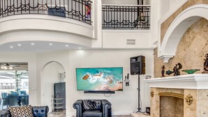 A spacious living area with a high ceiling, a large flat-screen TV mounted on the wall, and a fireplace with decorative items. - Golden Globe - Luxury on the Canal With Pool spa (Cape Coral)