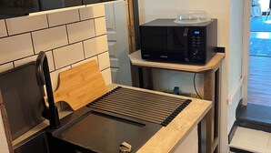 Una cocina con estufa a gas integrada, un microondas sobre una mesita y un lavamanos.