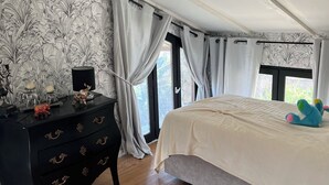 Un dormitorio con cama, piso de madera, cómoda negra y ventana con cortinas.