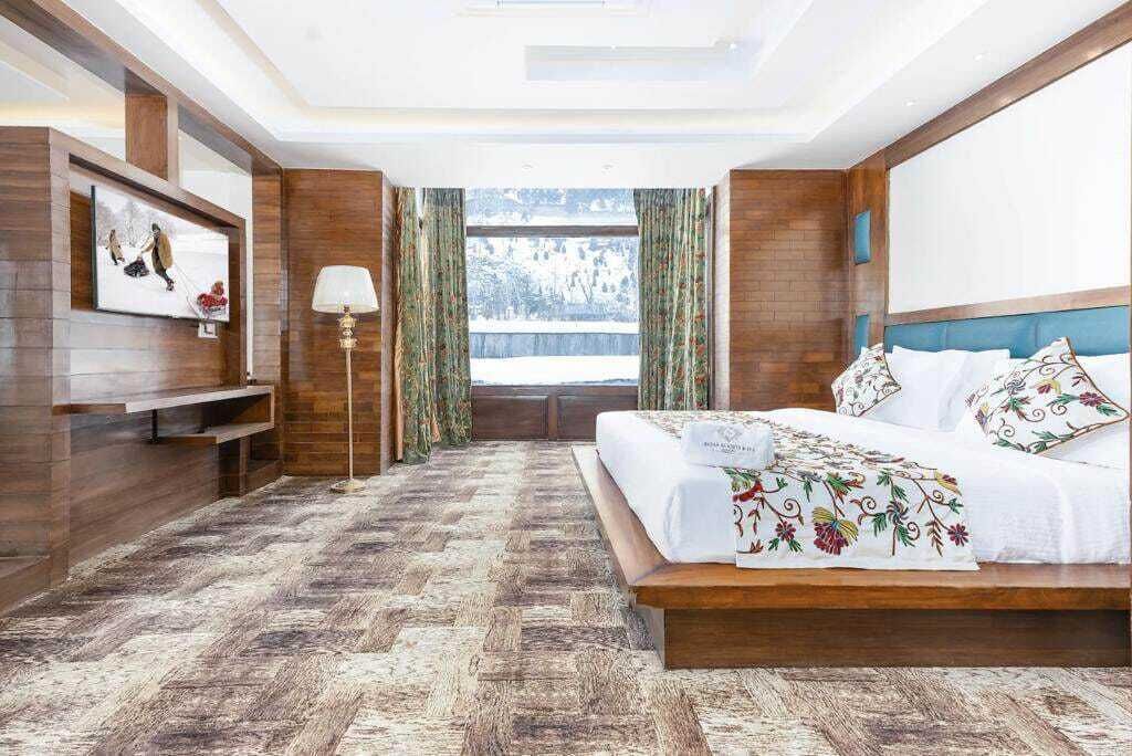 Quarto com cama grande, paredes de madeira, janela com cortinas e vista para uma paisagem nevada.