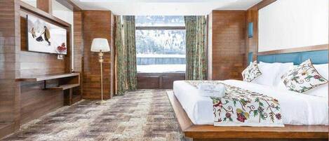 Quarto com cama grande, paredes de madeira, janela com cortinas e vista para uma paisagem nevada.