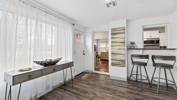 A modern kitchen with a wooden countertop, two barstools, and a dining area with a view of the living room. - Cozy vintage home in the heart of Riverside one block from golf, and much more (Wichita)