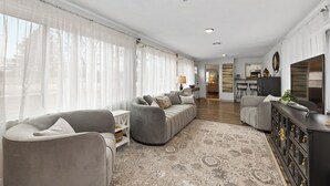 A spacious living room with a large sectional sofa, a smaller armchair, and a dark wooden cabinet. - Cozy vintage home in the heart of Riverside one block from golf, and much more (Wichita)