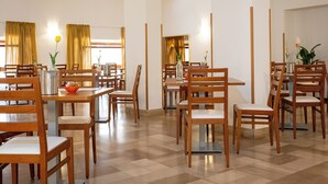 A spacious dining area with wooden tables and chairs, large windows with curtains, and a checkered floor. - Hotel Il Gabbiano (Alghero)