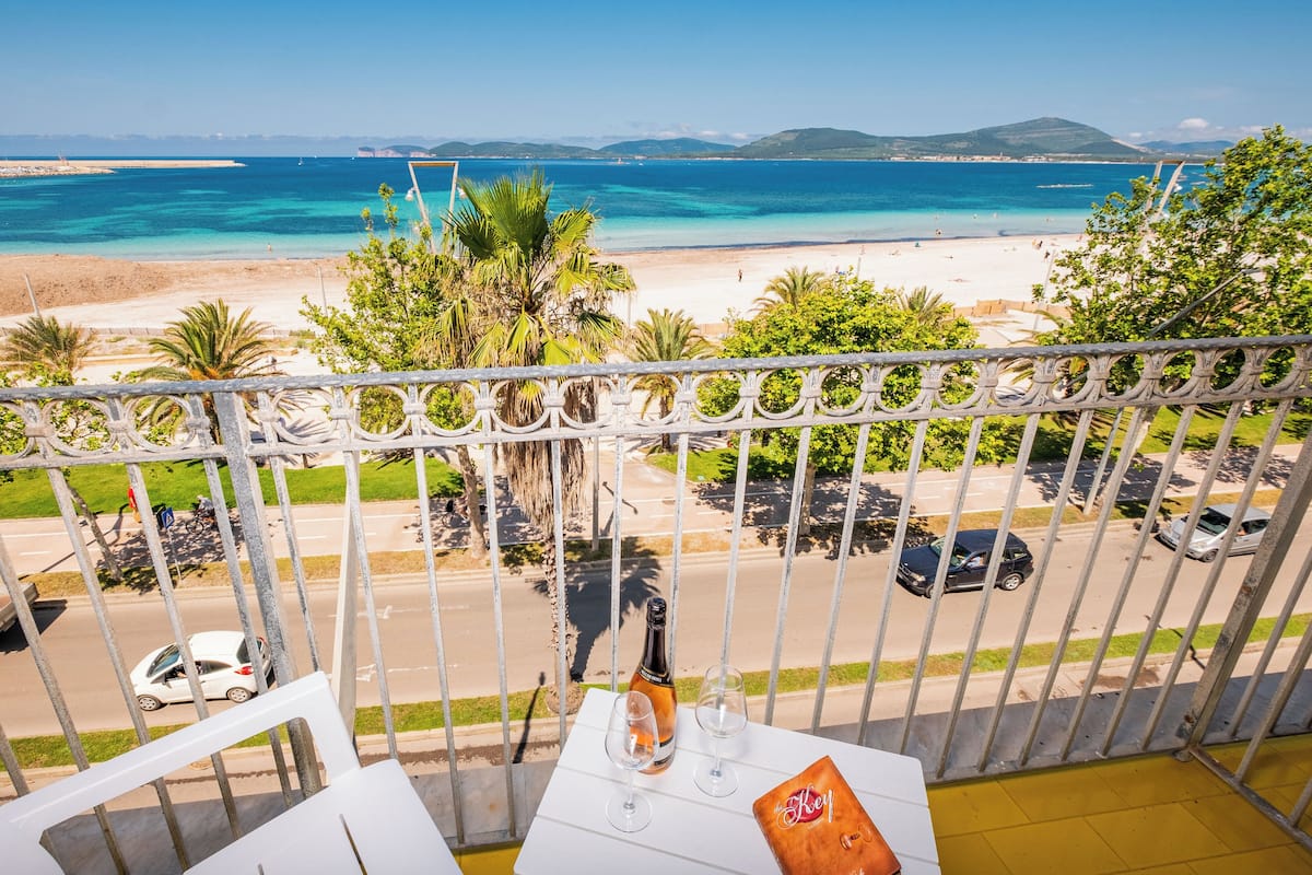 Un balcon donnant sur une plage et la mer, une bouteille de champagne et deux verres posés sur une table.