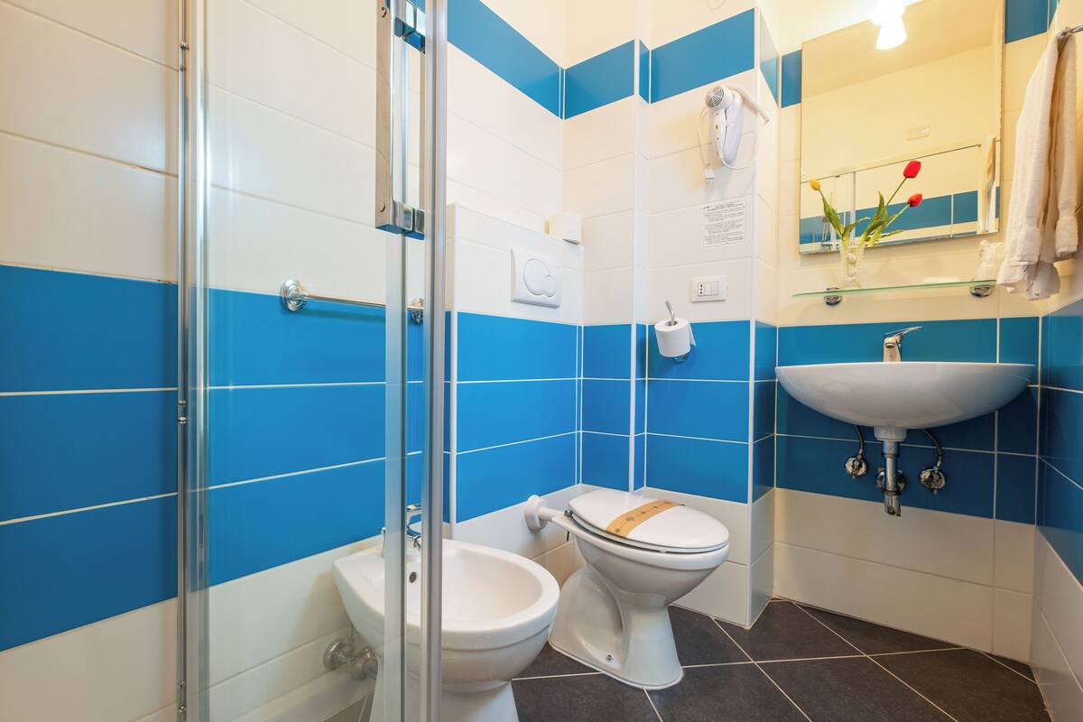 Une salle de bain avec des carreaux bleus et blancs, une douche en verre, des toilettes, un bidet et un lavabo.