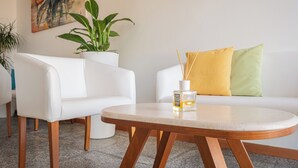 A modern living room with a white sofa, a round wooden table, and a potted plant. - Hotel Il Gabbiano (Alghero)