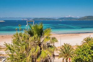 Una playa con aguas turquesas cristalinas, palmeras y una vista distante de montañas.