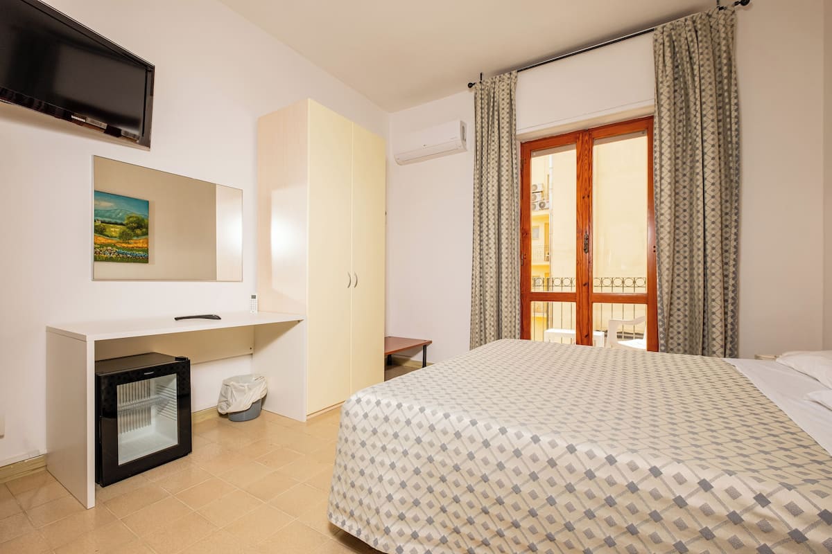 Une chambre d’hôtel avec un lit, un petit réfrigérateur, un bureau avec un miroir et une fenêtre avec des rideaux.