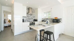 A modern kitchen with white cabinetry, a marble island, black bar stools, and a patterned backsplash. - Waterside Village - Sea View Apartment (Luz)