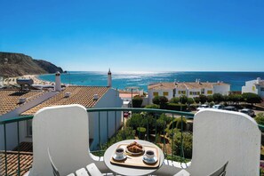 Un balcón con mesa lista para el desayuno y vistas a la costa.