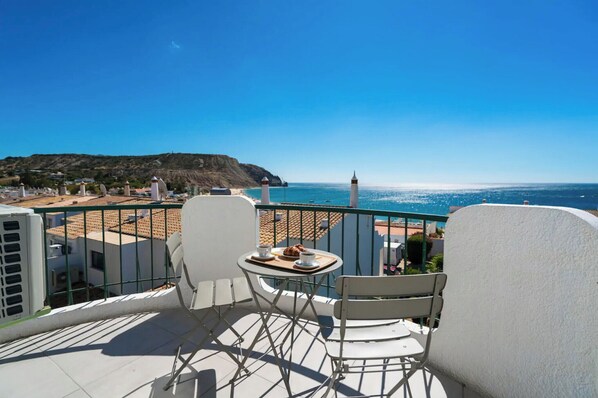 Un balcón con una mesa preparada para dos personas, con vista a una playa y al mar.