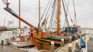 Ein hölzernes Boot liegt an einem Steg, mit einem Rettungsring und einem Schild, das eine tägliche Schifffahrtsverbindung anzeigt.