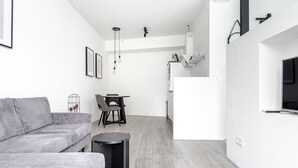A modern living room with a grey sofa, a small round table, and a dining area with a chair.