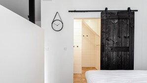 A bedroom with a bed, a wooden sliding door, a white wall, and a hanging clock.