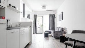 A modern kitchen with white cabinets and a coffee maker, a dining area with a table and chairs, and a living room with a sofa and a side table.