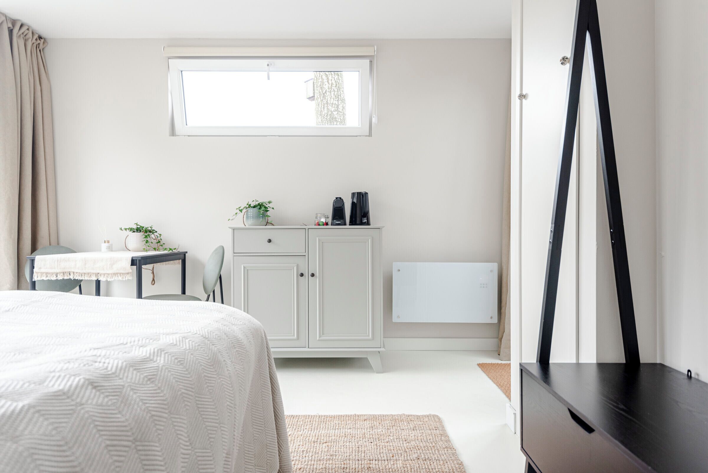 A bedroom with a bed, a desk, a cabinet, a radiator, and a window.