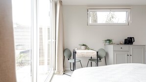 A bedroom with a large bed, a window, a small table with chairs, and a kitchenette area.