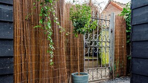 A bamboo fence with a metal gate, a large planter, and a building with a tiled roof.