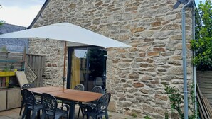 A stone building with a wooden table and chairs under a white umbrella. - L'escale - Longère en Campagne 6 Voyageurs, 3 Chambres (Pouldreuzic)