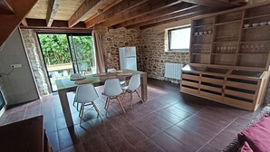 A dining area with a stone wall, a wooden table, and white chairs. - L'escale - Longère en Campagne 6 Voyageurs, 3 Chambres (Pouldreuzic)