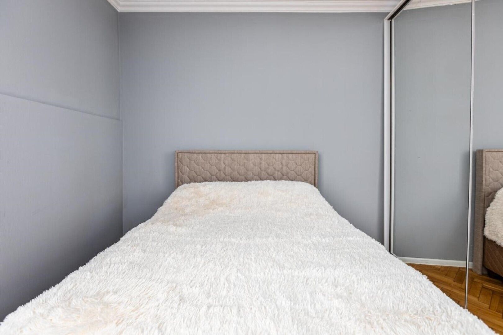 A bedroom with a bed, a mirror, and a light-colored wall.