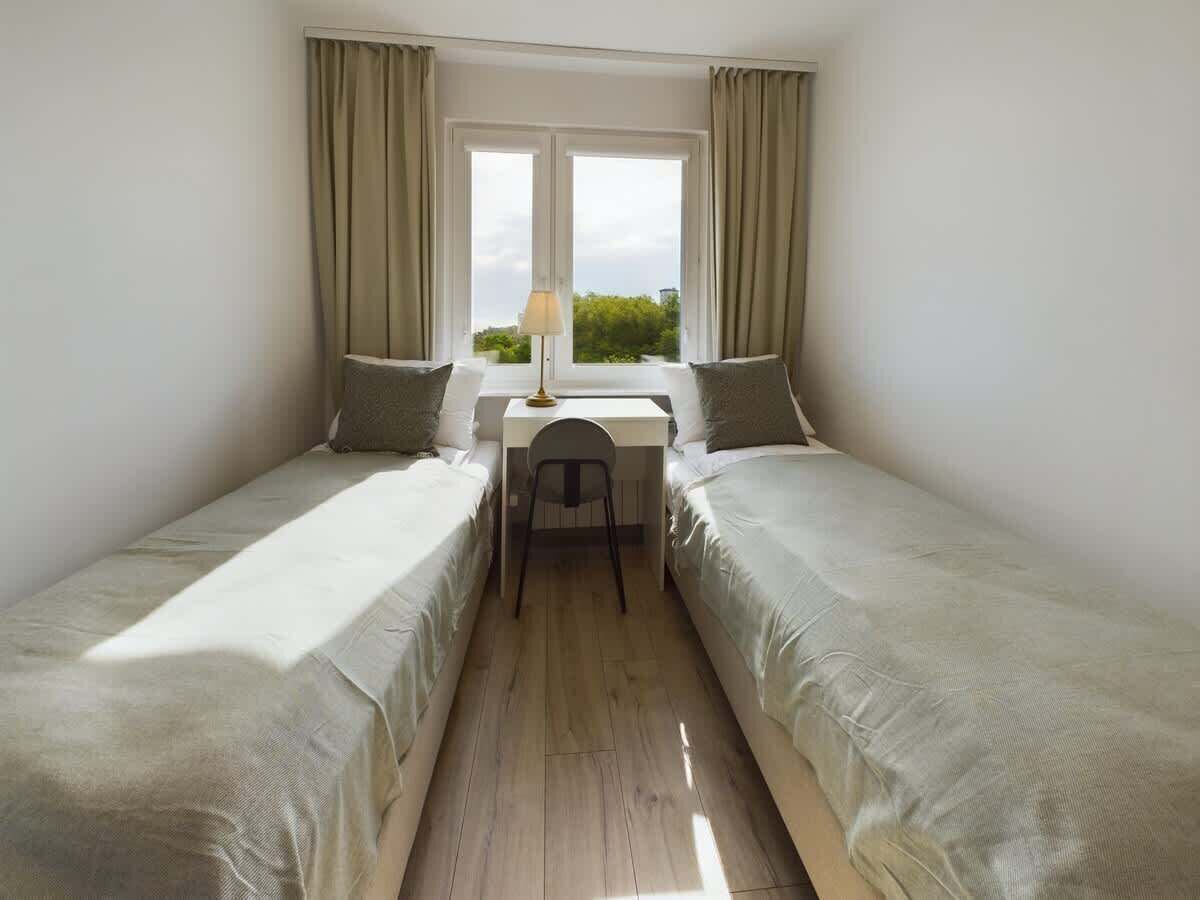 A small, well-lit room with two single beds, a desk, and a chair.