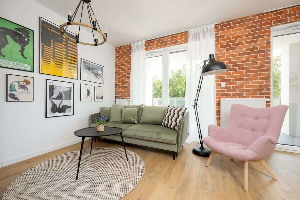 A cozy living room with green sofa, a circular coffee table, and a pink armchair, decorated with modern art and exposed brick walls, creating a stylish and warm ambiance.