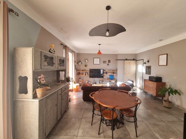 Une cuisine moderne avec un coin repas, comprenant une table et des chaises rondes en bois, un meuble encastré et une grande fenêtre qui laisse entrer la lumière naturelle.