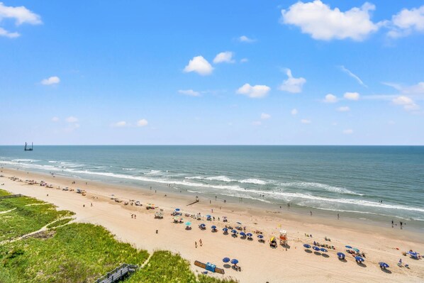 A beach with umbrellas and people, a lifeguard tower, and a clear sky.