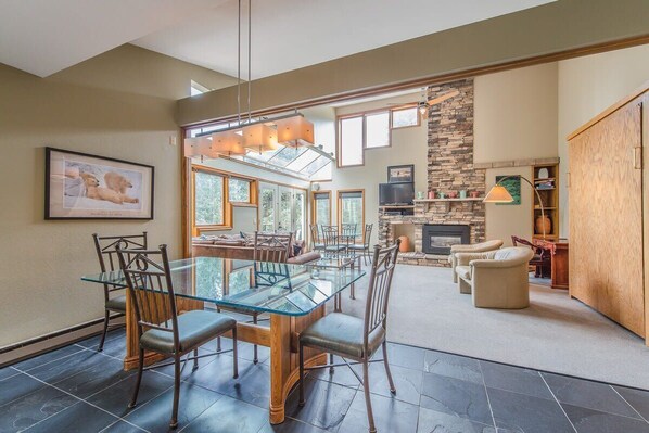 A spacious dining area with a glass table and chairs, a stone fireplace, and a view of the outdoors.