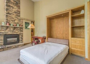 A bedroom with a bed, a wooden wardrobe, a fireplace, and a desk.
