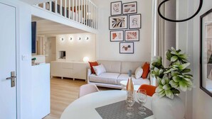 A modern living room with a staircase, a dining area with a table and chairs, and a sofa. - SUEDE PROMENADE – Duplex apartment at 1 min from the sea, 2 bathrooms (Nice)