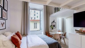 A hotel room with a bed, a desk, a chair, a TV, and a window with curtains. - SUEDE PROMENADE – Duplex apartment at 1 min from the sea, 2 bathrooms (Nice)