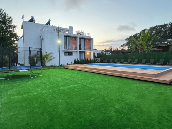 Una casa moderna con piscina, un trampolín y un césped bien cuidado.