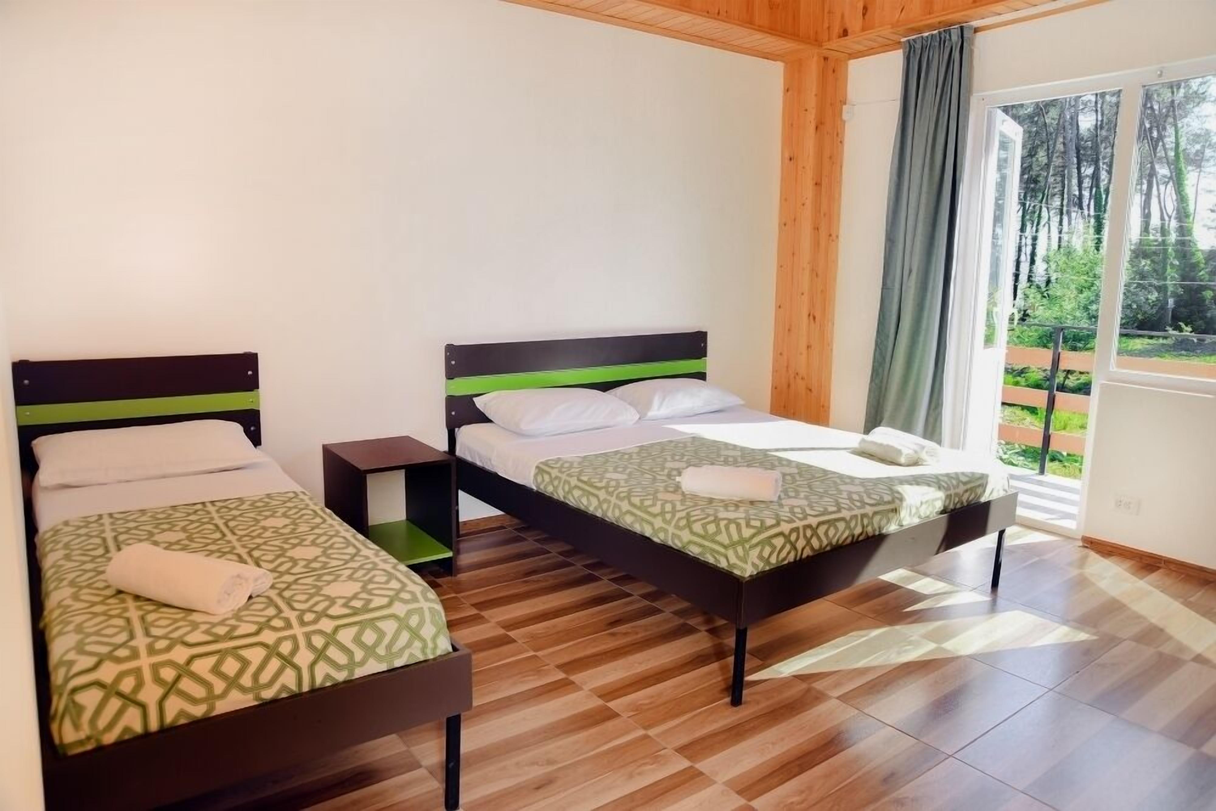 Quarto com duas camas, piso de madeira e janela com vista para árvores.